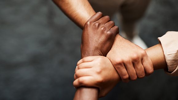 Arme von drei Personen, die fest miteinander verschränkt sind. 