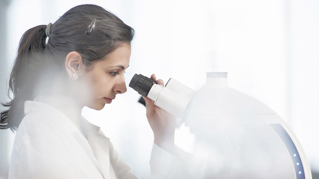 Frau schaut im Labor durch ein Mikroskop