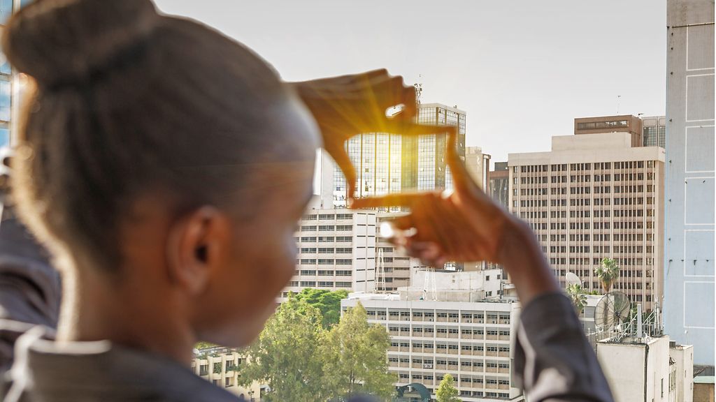 Junge Frau formt mit ihren Händen einen Rahmen für die Aussicht. Im Hintergrund die Skyline von Nairobi, Kenia.