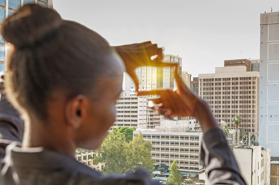 Junge Frau formt mit ihren Händen einen Rahmen für die Aussicht. Im Hintergrund die Skyline von Nairobi, Kenia.