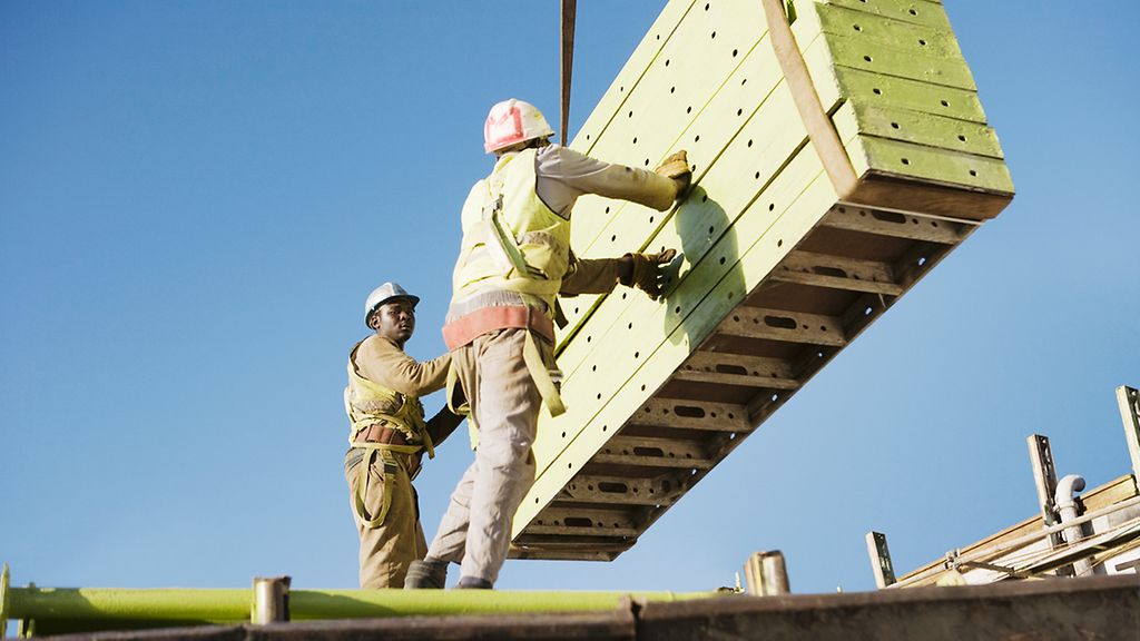 Workmen manoeuvre building materials on tower crane, Arbeiter manoevrieren Baumaterialien auf Turmdrehkran