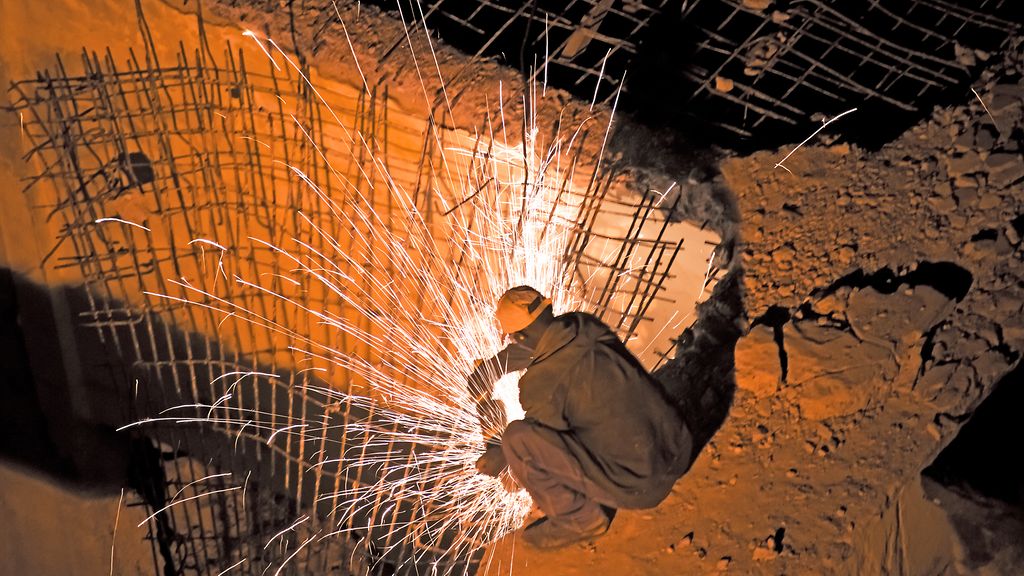 Construction worker working at night cutting reinforcement steel with a steel cut off saw.